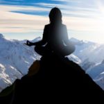 Frau sitzt im Yogasitz auf Bergspitze